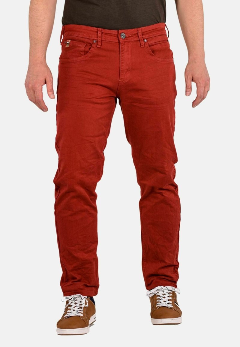 Jeans rojos ajustados con cinco bolsillos, botón de metal y costuras tonales. El material parece ligeramente texturizado y tiene un aspecto casual y desgastado.