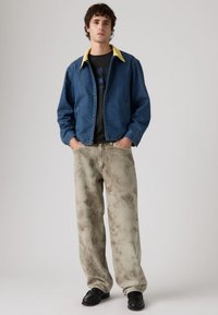 Τζιν μπουφάν σε μπλε με κίτρινο γιακά, συνδυασμένο με μπεζ και γκρι παντελόνια φαρδιάς γραμμής με σχέδιο και μαύρα παπούτσια. Casual εμφάνιση.