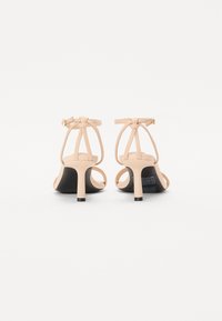 Nahé kožené sandály na podpatku s elegantním designem, tenkými popruhy, uzavíráním na kotníku a černou podrážkou s mírně zakřiveným podpatkem.