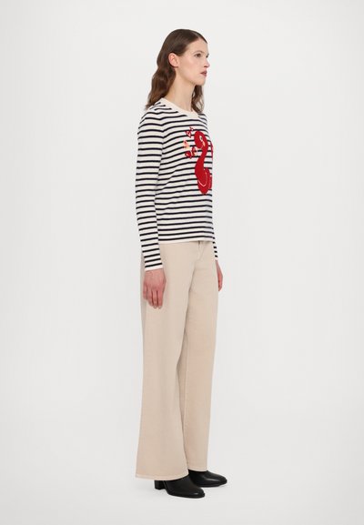 Striped long-sleeve sweater in cream and navy, featuring a red embroidered design. Paired with beige wide-leg pants and black heeled boots.