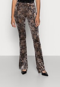 Ruskean käärmeennahkakuosiset, liehuvat housut, jotka on valmistettu pehmeästä, teksturoidusta kankaasta. Ominaisuuksiin kuuluu keskikorkea vyötärö ja hienovaraiset polvirei'ät, yhdistettynä mustiin, kärjettyihin korkokenkiin.