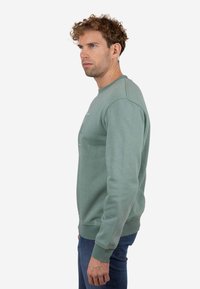 Sudadera de color verde claro hecha de mezcla de algodón, con puños y dobladillo acanalados, cuello redondo y un estampado sutil en la parte delantera.