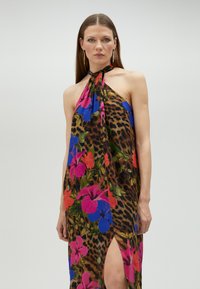 El vestido maxi de cuello halter presenta un estampado de leopardo con vibrantes patrones florales en rosa, azul y naranja. Tejido suave con una abertura lateral.