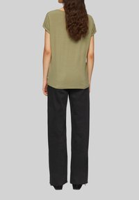 Oliwkowa bluzka z krótkim rękawem w zestawieniu z czarnymi, luźnymi spodniami z postrzępionymi nogawkami. Miękki materiał i swobodny fason.