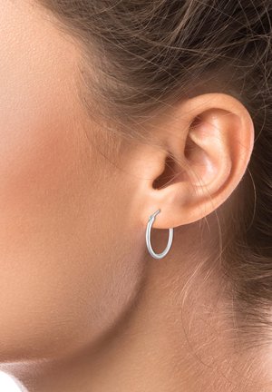 Boucle d'oreille en argent affichée sur l'oreille d'une personne, présentant une forme arrondie et une surface lisse et réfléchissante, mettant en valeur un design minimaliste.