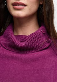 Hluboký fialový svetr s krkem do cowl, s texturovaným límcem, který má po straně dva kulaté knoflíky a hladké tělo. Měkký, pletený materiál.