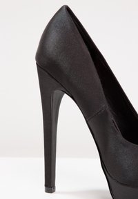 Escarpin noir à talon haut avec une finition satinée, un bout pointu et un talon stiletto fin. Présente un extérieur lisse et épuré.