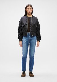 Jachetă bomber neagră cu material lucios și mâneci moi, asortată cu blugi albaștri ajustați și pantofi cu imprimeu leopard. Vedere frontală, fundal neutru.