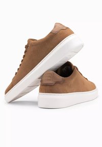 Baskets en suede marron avec une semelle en caoutchouc blanche, présentant un laçage à l'avant, des détails cousus et un accent de marque au niveau du talon.
