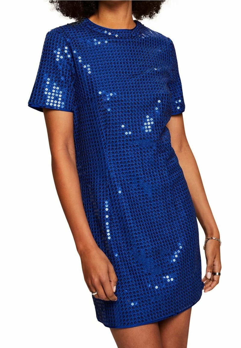 Femme portant une robe à paillettes bleu roi à manches courtes, au-dessus du genou, avec un décolleté rond et un motif texturé.