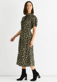Leopard print dress in shades of green and black, featuring a collar, short sleeves, and a flowing mid-length design. Black ankle boots.