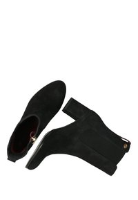 Botas de tobillo de ante negro con puntera redonda, paneles laterales elásticos y tacón cuadrado. Incluyen una cremallera dorada y un acento decorativo.