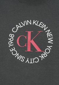 Sivé bavlnené tričko s kruhovým bielym a ružovým grafickým potlačou, na ktorej je napísané "CALVIN KLEIN NEW YORK CITY SINCE 1968" a v strede "cK".