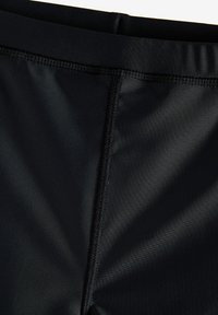 Shorts de sport noirs avec une taille élastique lisse et des coutures flatlock, fabriqués en tissu évacuant l'humidité pour le confort et la durabilité.