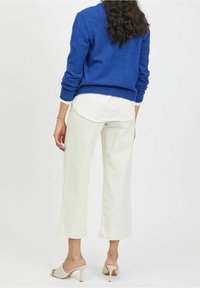 Modrý pletený svetr, bílý vrstvený top, světlé široké kalhoty a béžové otevřené podpatky. Texturovaný pletený materiál a čisté linie.