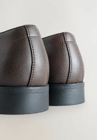 Bottes en cuir marron avec une finition texturée, comportant des coutures verticales et une épaisse semelle en caoutchouc noir. Design arrondi à l'arrière.
