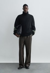 Čierny rolák s vyšívaním zeleného listu na rukávoch, skombinovaný s tmavo hnedými nohavicami širokého strihu a čiernou kabelkou na ruku.