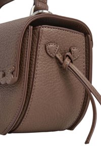 Brūns teksturēts ādas rokassomu ar mezglotiem siksnām un strukturētu vāku, parādīta tuvplānā uz balta fona.