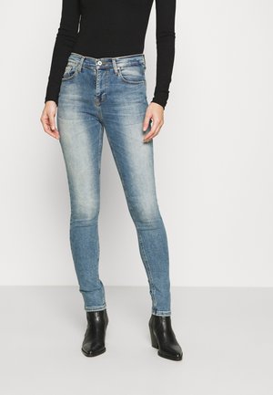 Jeans skinny en denim bleu clair, avec un effet délavé, design à cinq poches, fermeture par bouton et silhouette élégante, associés à des bottines noires.