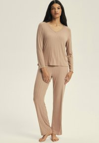 Lightweight ribbed pajama set in soft beige. Long-sleeve top with a V-neck and matching pants. Smooth texture and relaxed fit.