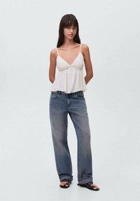Hvid ærmeløs top med V-udskæring og samlet kant, parret med lyseblå baggy jeans. Sandaler med sorte stropper fuldender outfittet.