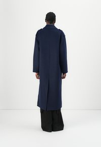 Palton lung din lână navy, cu croială dreaptă, dotat cu o ventilație pe spate, mâneci largi și epoleți pe umeri. Design curat și minimalist.