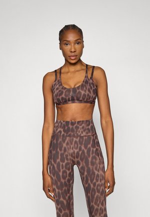 Brązowy top sportowy w zwierzęcy wzór z regulowanymi ramiączkami, zestawiony z legginsami z wysokim stanem. Gładka faktura i dopasowany krój do aktywnego noszenia.