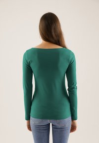 Langarmat, aansluitend top in groene katoen, met een brede ronde hals en zachte textuur, gecombineerd met lichtblauwe jeans.