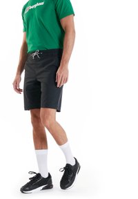 Schwarze Shorts mit einem elastischen Bund und Zugband, kombiniert mit einem grünen T-Shirt und schwarzen Sneakers, getragen mit weißen Socken.