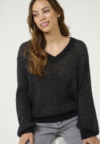 Svart, löst stickad tröja med V-ringning och långa ärmar. Har en subtil metallictråd som skapar en strukturerad look.