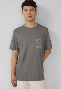 Grijze katoenen T-shirt met korte mouwen, een ronde hals en een gemusterde borstzak. Zachte stof, relaxte pasvorm en een minimalistisch ontwerp.