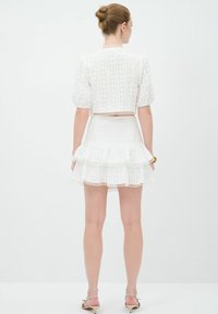 Weißes Baumwollkleid mit Puffärmeln, tailliertem Oberteil und gestuftem Rüschenskleid, verziert mit Spitzenbesatz und subtilen strukturierten Mustern.