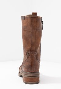 Brązowy skórzany but za kolano z teksturowanym wzorem i bocznym zamkiem błyskawicznym. Posiada obcas w kształcie stosu oraz subtelne akcenty wzorów po bokach.