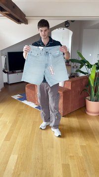 Svijetloplave traper šortse s pocepanim rubom i džepovima, s oznakom Levi's, koje drži osoba u ležernom outfitu na drvenom podu.
