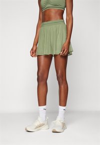 Skort activo verde con un diseño acampanado, hecho de un tejido ligero, combinado con zapatillas blancas y calcetas a rayas.