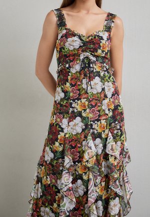 Frau trägt ärmelloses schwarzes Kleid mit buntem Blumenmuster und Ösen-Spitzen-Details, geraffter Brustpartie und Volant-Ärmeln.