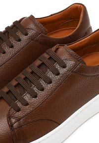 Bruine leren sneakers met een gestructureerd oppervlak, ronde neus, bruine veters en een witte rubberen zool. Eenvoudig ontwerp met minimale accenten.