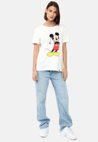 Hvid bomulds t-shirt med en grafik af Mickey Mouse iført røde shorts og gule sko. Sammen med lyseblå denim jeans og hvide sneakers.