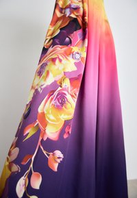 Langes Kleid mit einem lebhaften Blumenmuster in Abstufungen von Pink und Lila. Der Stoff erscheint glatt und hat eine weiche Textur.