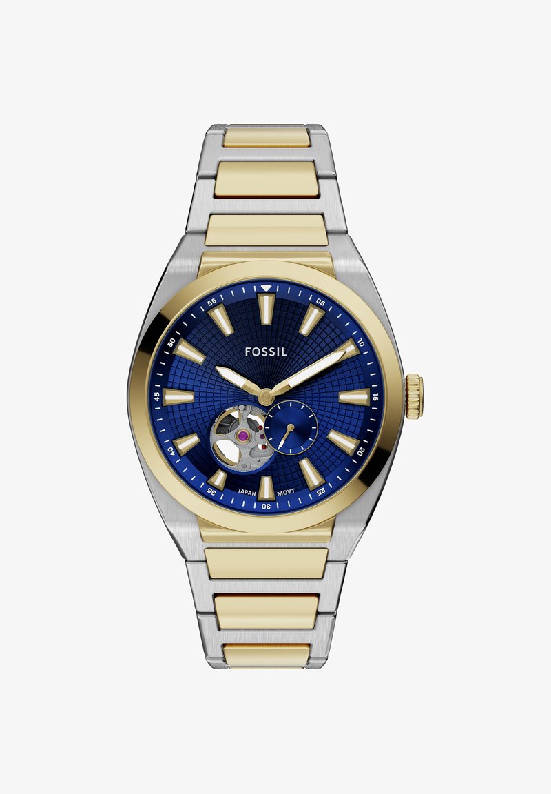 Montre-bracelet Fossil avec cadran bleu, bracelet métal doré et argenté, index dorés, affichage « open heart » et petite seconde à 5 heures.