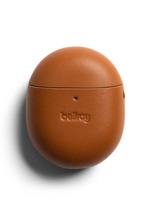 Custodia compatta e rotonda in pelle marrone con "bellroy" impresso sul davanti, progettata per contenere auricolari wireless, che proietta un'ombra su sfondo bianco.