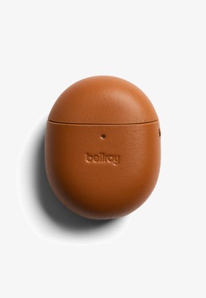 Étui compact, rond en cuir marron avec le logo "bellroy" embossé sur le devant, conçu pour contenir des écouteurs sans fil, projetant une ombre sur un fond blanc.