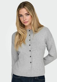 Siva rebrasta pletena jopa z okroglo izrezom, sprednjim zapiranjem na črne gumbe in dolgimi rokavi.