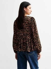 Blouse à imprimé léopard avec des manches longues, ourlet volanté et coupe décontractée, fabriquée en tissu léger dans des tons de marron et de noir. Associée à un jean.