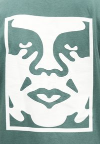 Στυλιζαρισμένο λευκό γραφικό προσώπου με κλειστά μάτια, μύτη, χείλη και μάγουλα σε πράσινο υφασμάτινο φόντο.