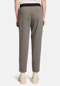 Pantalons à carreaux gris et noirs avec une coupe fuselée, dotés d'une taille élastique noire et de deux poches arrière. Stylés avec des bottines beiges.