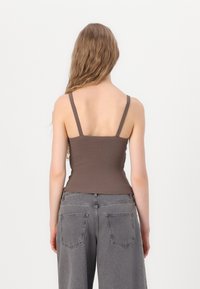 Brun ribbet tanktop med tynne stropper, tettsittende design. Kombinert med høyhårede grå vide bukser med baklommer.