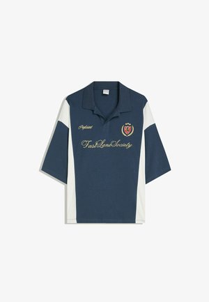 Mornarsko modra polo majica z belimi stranskimi ploščami. Ima vezeno logotip in besedilo v zlati barvi. Kratki rokavi in klasična zasnova ovratnika.