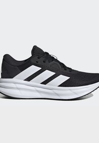 Chaussure de course noire avec une semelle blanche amortie et trois bandes blanches sur le côté, vue de l'extérieur.