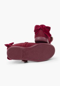 Scarpe in velluto bordeaux con punta rotonda, cinturino alla caviglia e decorazione a fiocco. Suola in gomma testurizzata con scanalature orizzontali per una maggiore aderenza.